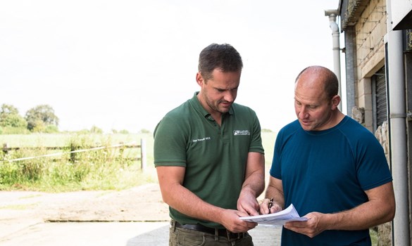 Male vet and farmer stood reviewing data on a printout next to a farm building